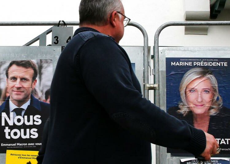 Seorang pria berjalan melewati poster kampanye presiden dari Presiden Prancis dan kandidat tengah untuk pemilihan kembali Emmanuel Macron dan kandidat presiden sayap kanan Prancis Marine Le Pen di Anglet, barat daya Prancis, Rabu, 8 April 2022.