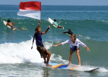 Dua peselancar wanita mengenakan pakaian kebaya sambil mengibarkan bendera Merah Putih saat beratraksi di Pantai Kuta, Badung, Bali, Sabtu (16/4/2022). Atraksi selancar untuk menyambut Hari Kartini itu sekaligus sebagai daya tarik wisata guna membangkitkan pariwisata Bali yang terdampak pandemi COVID-19.