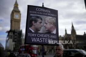 Seorang pengunjuk rasa anti-Boris Johnson mengangkat plakat dengan gambar dirinya dan Menteri Keuangannya Rishi Sunak, berlatar belakang Menara Elizabeth, yang dikenal sebagai Big Ben, dan Gedung Parlemen, di London, Rabu, 9 Februari 2022.