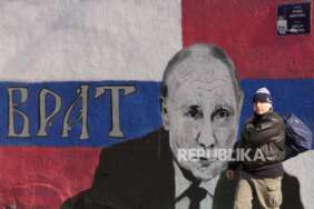 Seorang pria melewati mural yang menggambarkan Presiden Rusia Vladimir Putin, yang berbunyi: