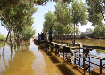 Siswa menggunakan bangku sekolah untuk menyeberangi banjir di sekolah yang terendam air, di distrik Mirpur Khas, provinsi Sindh, Pakistan, 10 Oktober 2022. Menurut otoritas manajemen bencana, sekitar 160 jembatan dan 5.000 km (3.200 mil) jalan hancur atau rusak, 3,5 juta hektar tanaman terpengaruh, dan sekitar 800.000 ternak hilang. Lebih dari 33 juta orang terkena dampak banjir, kata Menteri Perubahan Iklim negara itu Sherry Rehman.