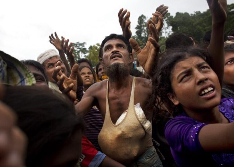 Seorang pria Rohingya mengulurkan tangannya untuk mendapatkan makanan yang dibagikan oleh sukarelawan lokal, dengan kantong beras kembung yang dimasukkan ke dalam rompinya di Kutupalong, Bangladesh, 9 September 2017. Perdana Menteri Bangladesh mengatakan Senin bahwa masa tinggal yang berkepanjangan lebih dari 1 juta Pengungsi Rohingya di kamp-kamp yang padat di negara itu telah menjadi masalah keamanan dan stabilitas.
